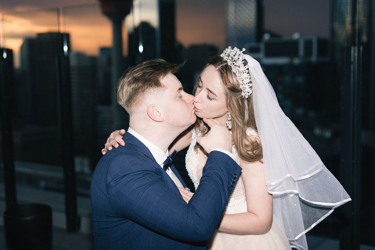 A groom kissing the bride's cheek on a Calgary rooftop at sunset