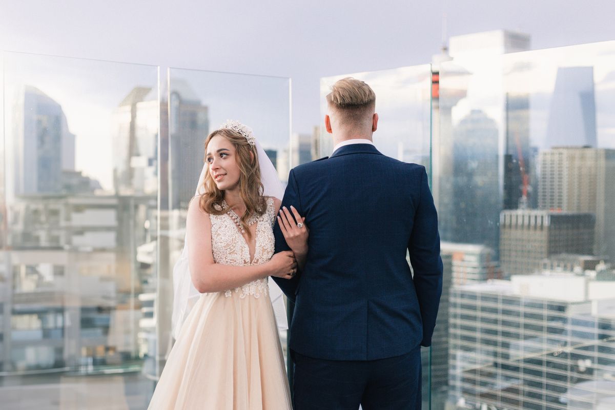 A bride glancing back over her shoulder beside the groom, downtown Calgary behind them
