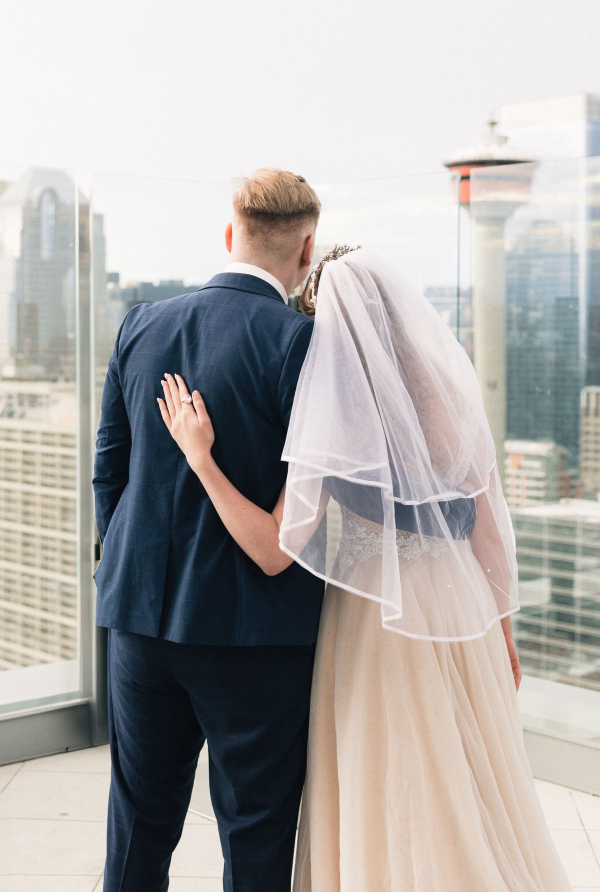 The bride and groom seen from behind on a rooftop, the Calgary Tower ahead