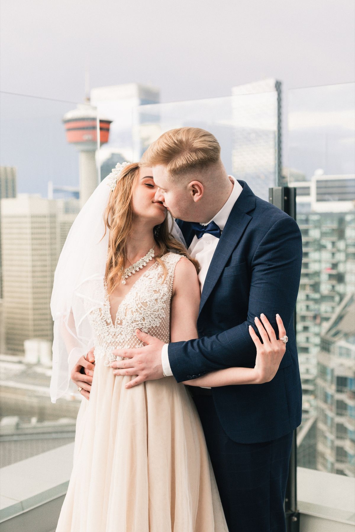 A bride and groom kissing on a rooftop with the Calgary Tower behind them