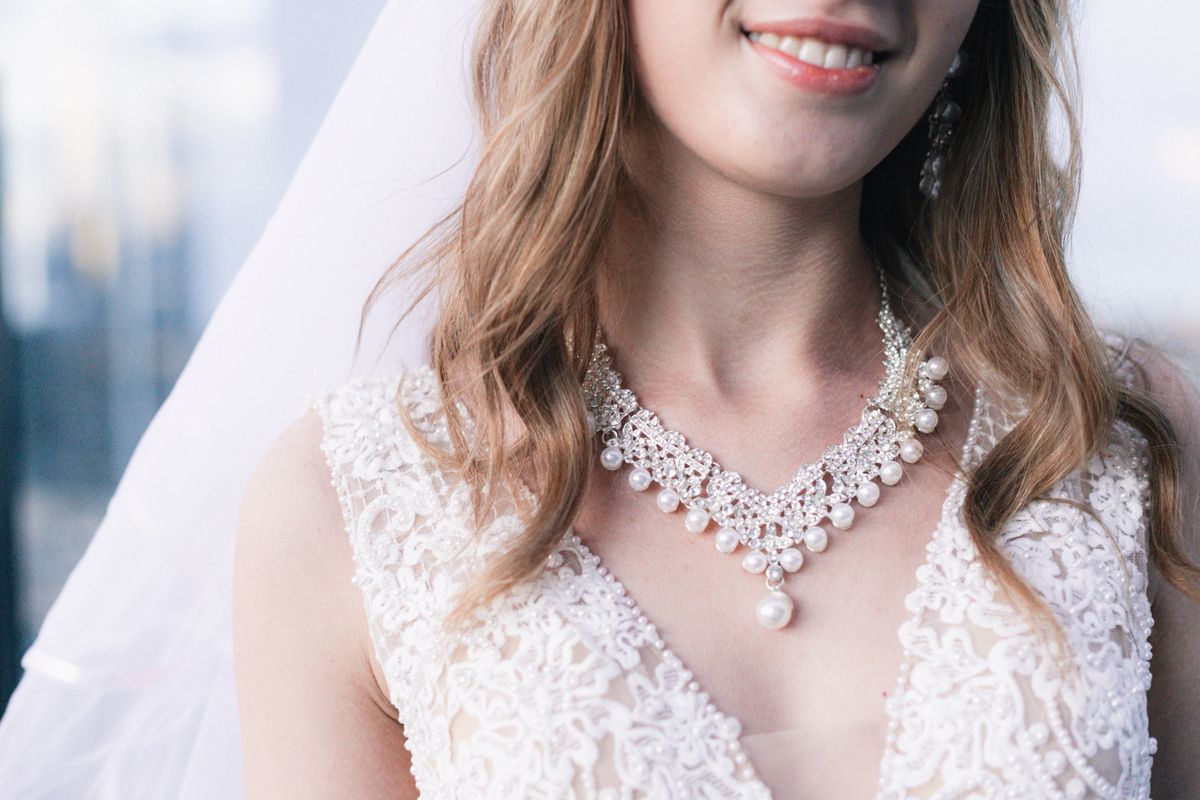 A close detail of the bride's pearl necklace and lace gown