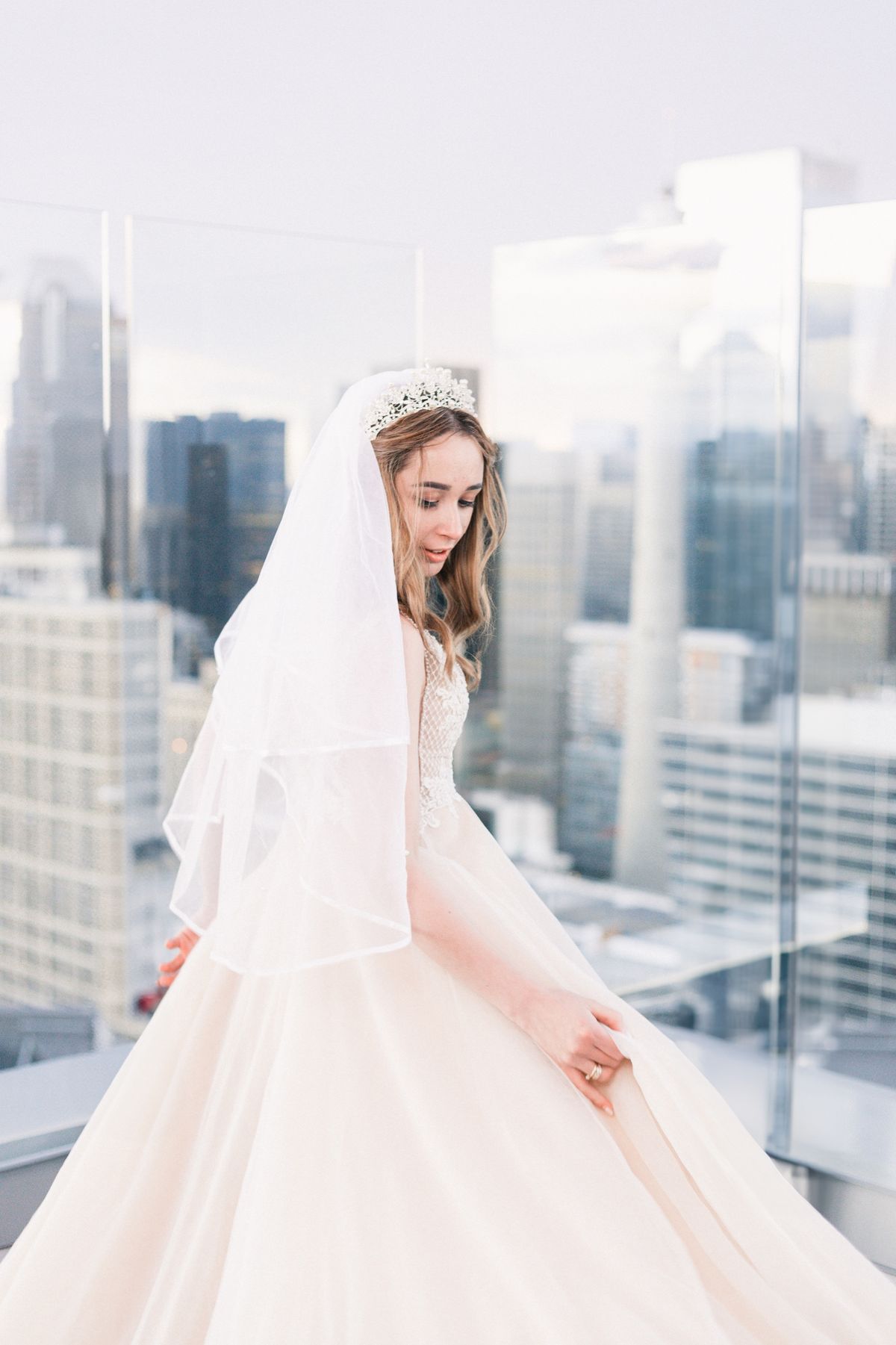 A bride looking down at her gown on a rooftop above downtown Calgary