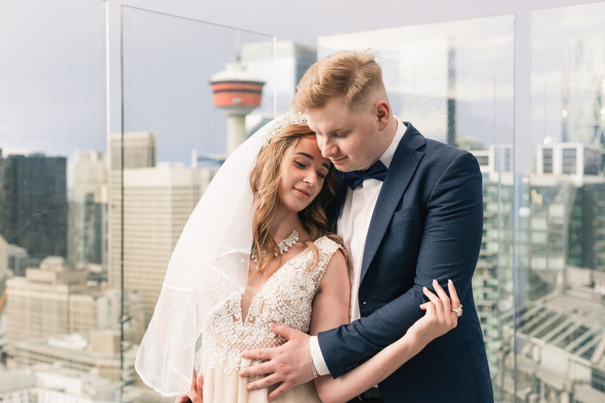 A groom holding the bride close on a rooftop with the Calgary Tower behind them