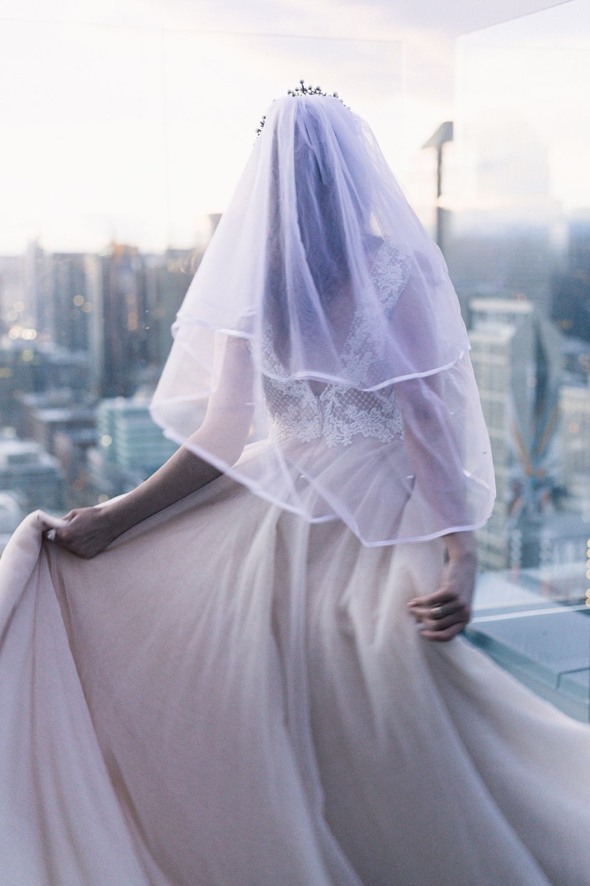 A bride from behind in her veil, looking out over the city